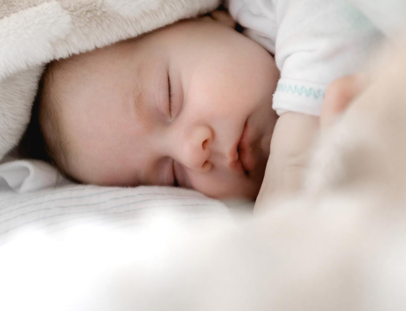 Ein Baby, das unter einer Decke schläft und die beruhigende Wirkung der craniosacralen Osteopathie erlebt.